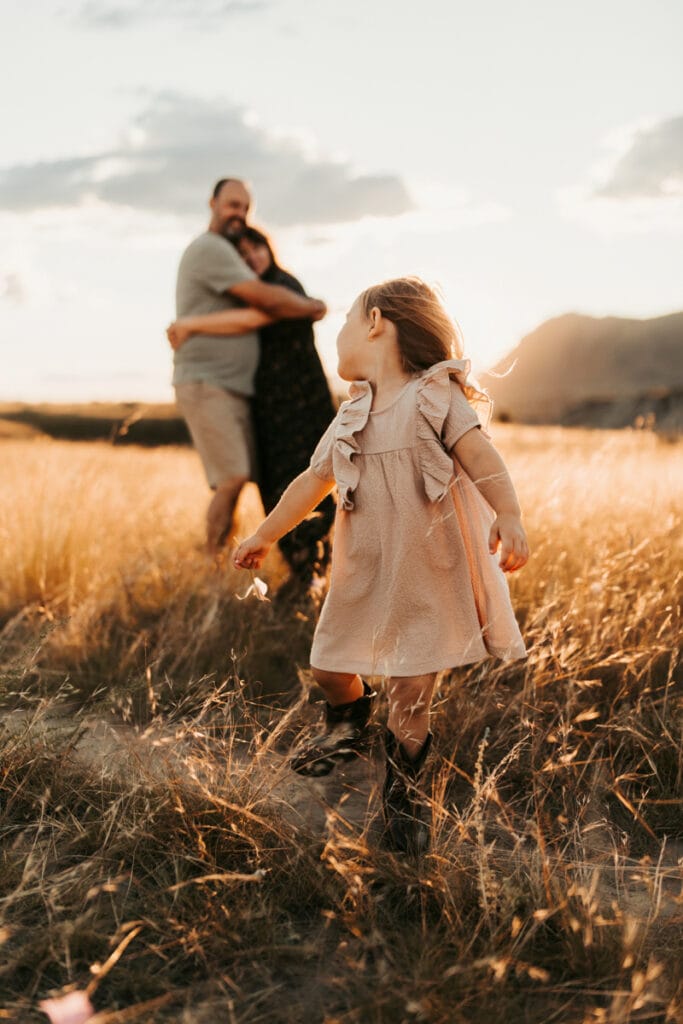 Family Photographer, little girl playing in field around her parents
