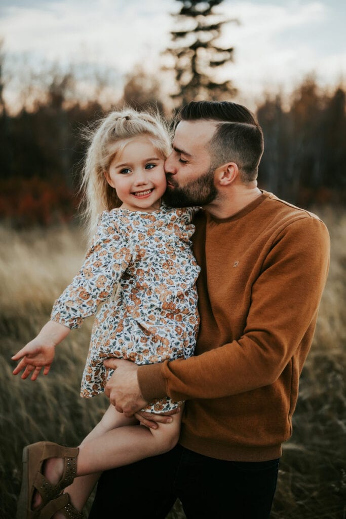 Family Photographer, father holding daughter up and kissing her cheek